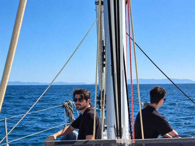 Christopher Scott aboard a sailboat, with open water and mountains in the background.